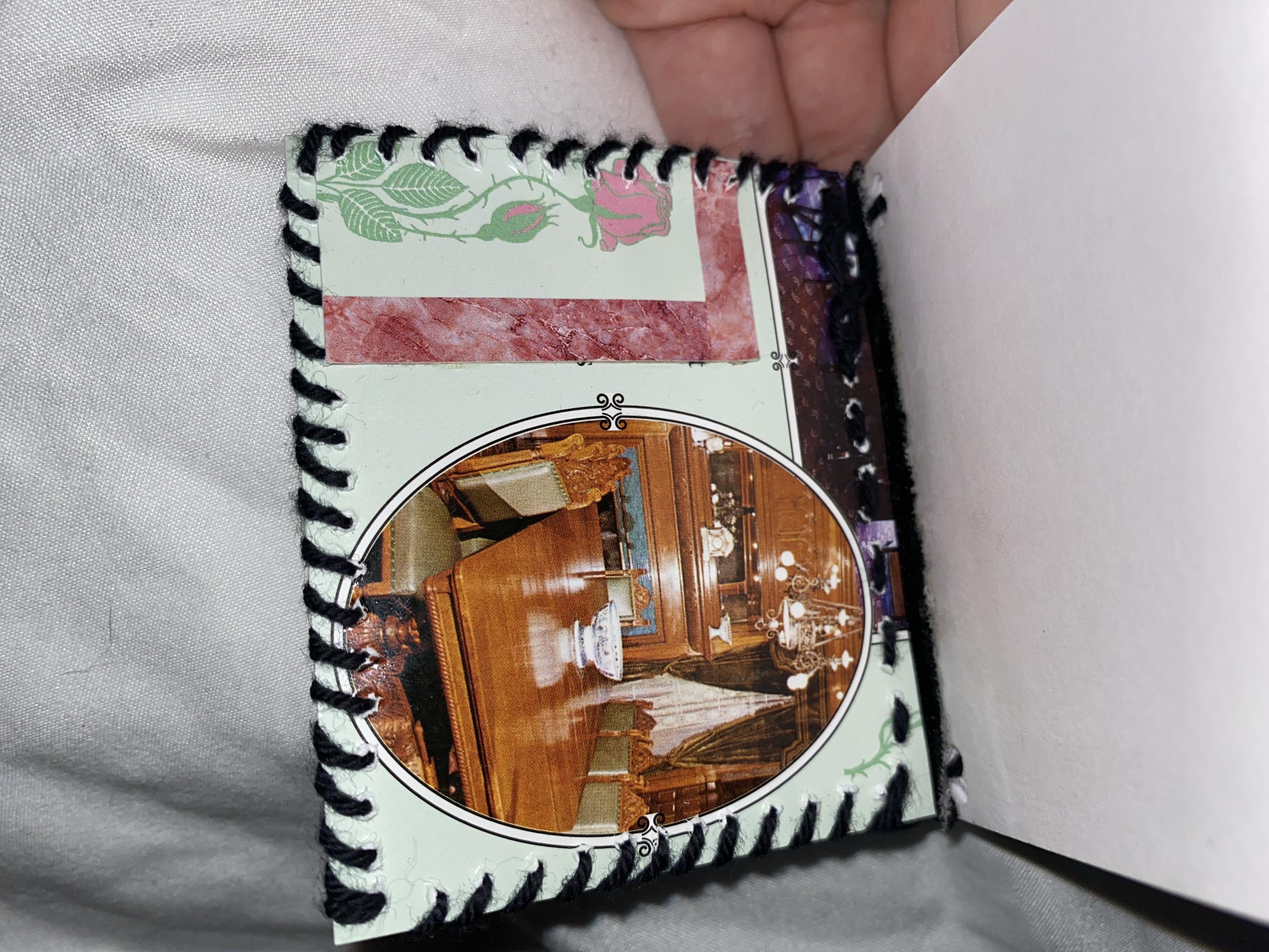 An open handmade book cover featuring a decorative border and an oval picture of a wooden dining table set in an ornate room.